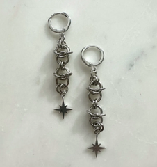 Pair of silver hoop earrings with chain and star charms on a marble surface
