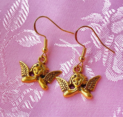 Gold angel-shaped earrings on a pink and white patterned background