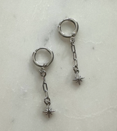 Pair of silver hoop earrings with chain and star-shaped charms on a light gray background