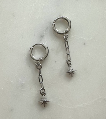Pair of silver hoop earrings with chain and star-shaped charms on a light gray background